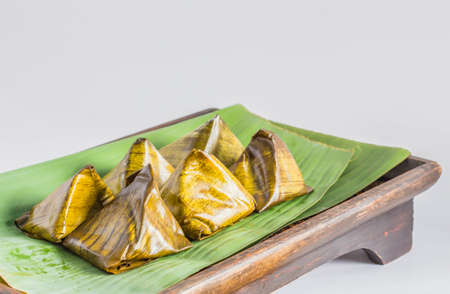 Dessert wrapped in banana leaves on the old wooden tray.