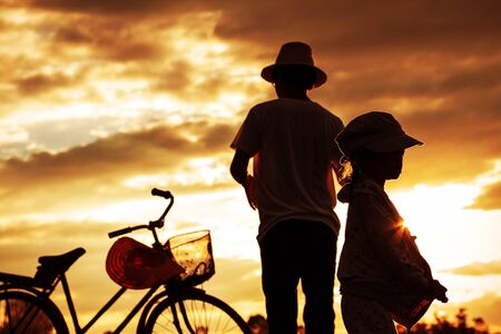 Father and son standing back with silhouettes at sunset.の写真素材
