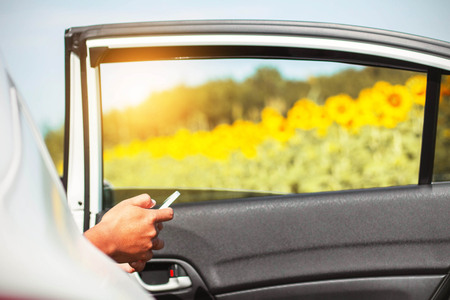 Travelers checks mobile phones on car at sunflower field.の写真素材