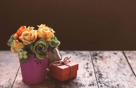 Vase of roses with a gift on the table.の写真素材