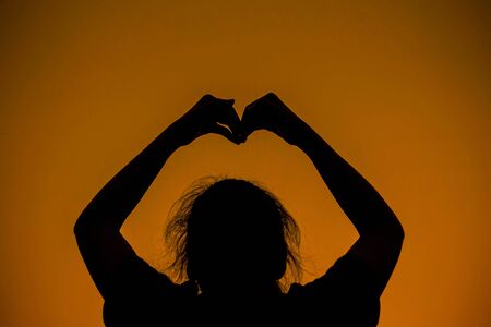 Woman with symbol of love in the sky at sunset.の写真素材