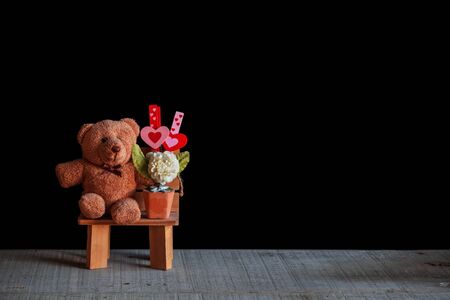 Teddy bears and hearts on a chair with a black background.の写真素材