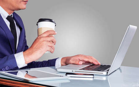 Young businessman holding a cup of coffee and using a computer.の写真素材