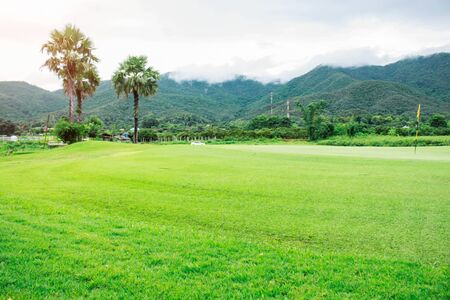 green grass of the golf course with mountains and skies.の写真素材