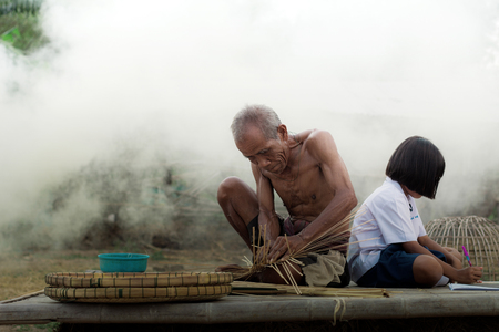 Old man and girls are weaving bamboo baskets on a litter.の写真素材