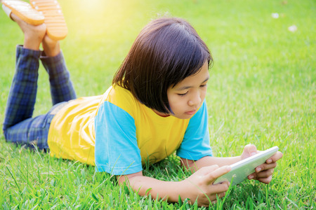 Asian girl are using tablet on lawn in park.