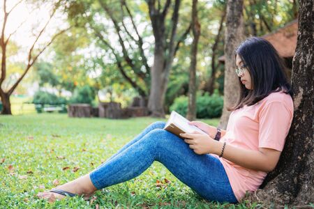 Asian girl are reading a book on lawn in the park.の写真素材