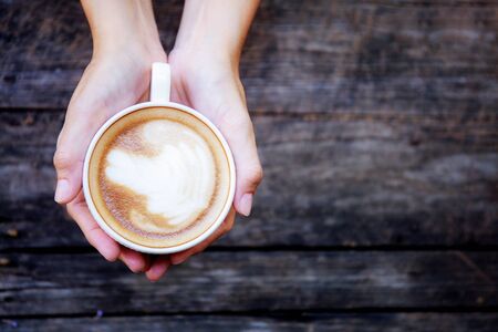 Hands holding coffee cup with wooden table background.の写真素材