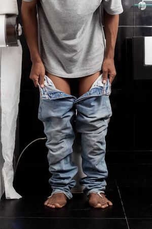Young man is removing jeans in the bathroom.の写真素材