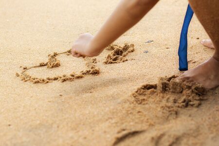 Hand with heart on sand at the sea.の写真素材