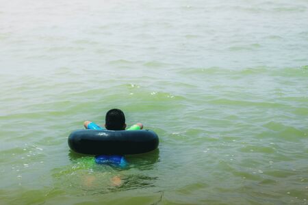 Boy with a rubber ring is playing the sea.の写真素材