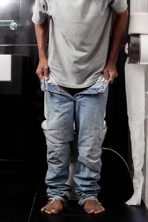 Young man is removing jeans in the bathroom.の写真素材