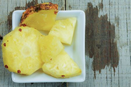 Pineapple of pieces on dish with a wooden background.の写真素材