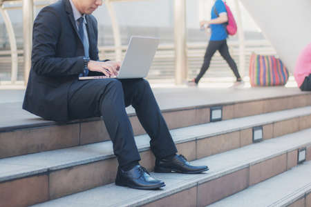 Young businessman using computer sitting on stairs.の写真素材
