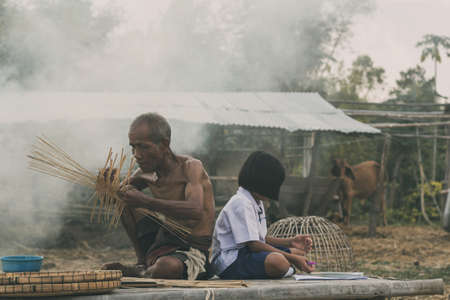 Old man and girl is sitting on a bamboo mat in the countryside.の写真素材