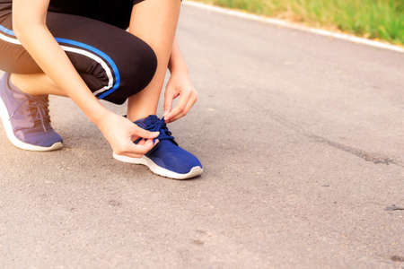 The girl is tying a shoe string on street.