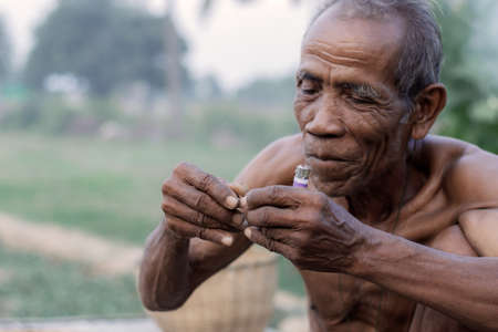 Old man are cigarette in field of Thailand.の写真素材