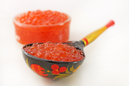 Red caviar in a bowl over white background. Wooden spoon painted in traditional style Khokhloma with natural caviar. Traditional souvenir from Russia.の写真素材