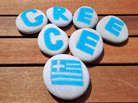 Greece country name painted on the stones on wooden plank background. Inscription on the sea stones.の写真素材
