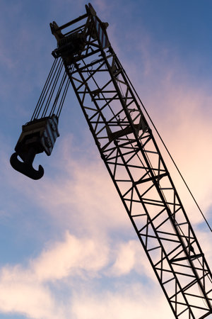 A silhouette shot of a crane hook against a blue sky with clouds