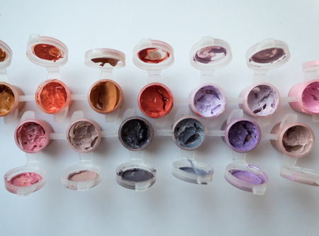 Paints flatlay on white background. Orange, yellow, lilac, broun. Top view.