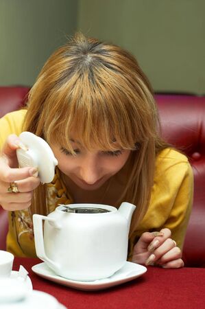 curious pretty girl looking into teapot with brewing teaの写真素材