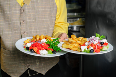 waiter at restaurant kitchen holding order of two dishesの写真素材