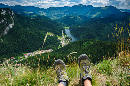 Somebody is sitting at the edge of cliff in mountains, showing his feet wearing hiking shoes. First person shoot. Retezat area, Carpathians, Romaniaの写真素材