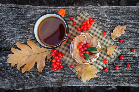 Romantic autumn still life with basket cake, cup of tea, rowan berries and leaves at wooden board, top viewの写真素材