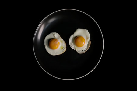 Two fried eggs on a black plate on a black background. AI generative imageの素材