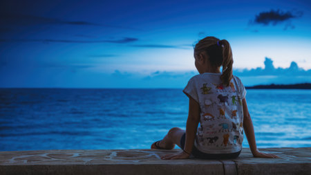 A young girl sitting on a ledge looking out at the ocean, AIの素材