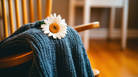 Cozy knitted blanket draped over a wooden chair with a daisy resting on top, AIの素材
