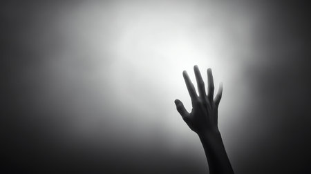 A hand reaches towards a bright light, creating a dramatic silhouette against a foggy backdrop, AIの素材