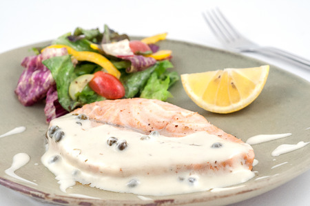 Grilled salmon with white sauce, vegetables and lemon isolated on whiteの写真素材