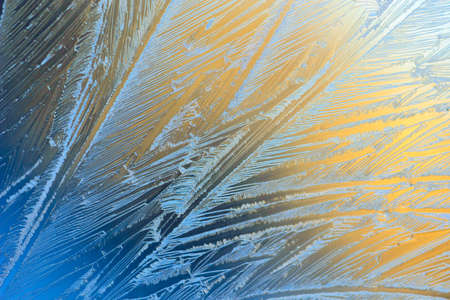 Window glass covered with ice pattern against sunsetの写真素材