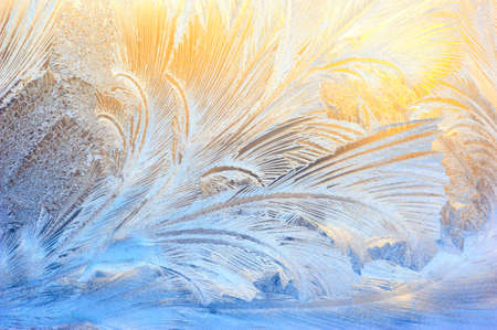 Window glass covered with ice pattern against sunsetの写真素材