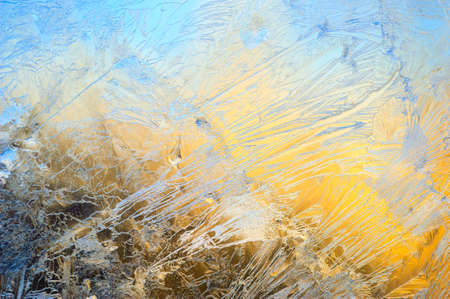 Window glass covered with ice pattern against sunsetの写真素材