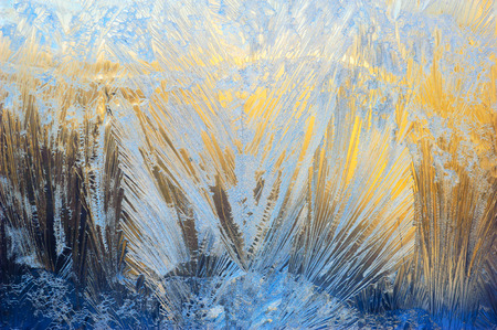 Window glass covered with ice pattern against sunsetの写真素材