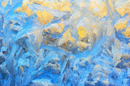 Window glass covered with ice pattern against sunsetの写真素材