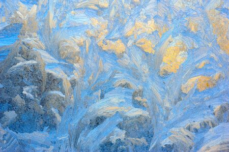 Window glass covered with ice pattern against sunsetの写真素材