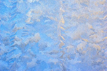 Window glass covered with ice pattern against sunsetの写真素材