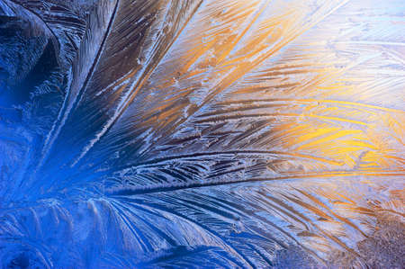 Window glass covered with ice pattern against sunsetの写真素材