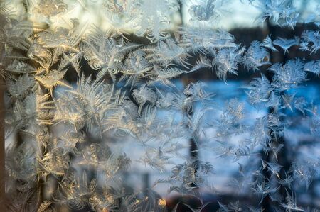 Window glass covered with ice pattern against sunsetの写真素材