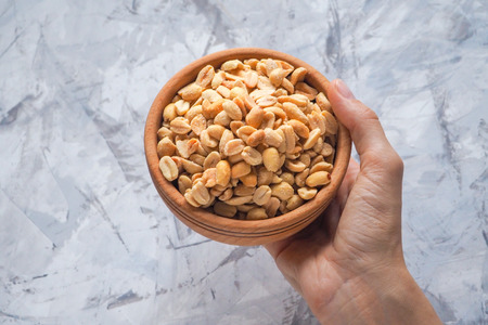 Roasted salted peanuts in hand. Roasted nuts in a bowl.