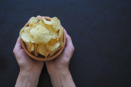 Woman's hands holding potato chips on a dark background.の写真素材
