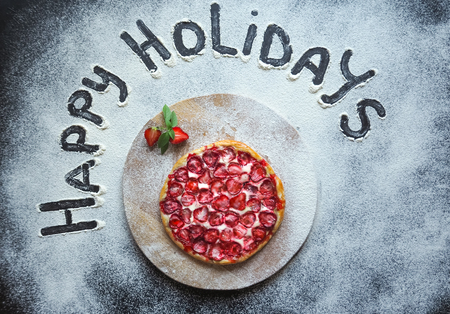 Strawberry cake and "happy holidays" sign on the black tableの写真素材
