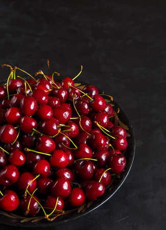 Red cherries in a plate on a black table. Top view. Copy spaceの写真素材