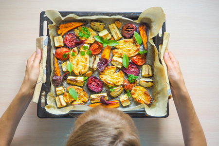 Woman's hands holding an old pan with baked vegetables. Top view.の写真素材