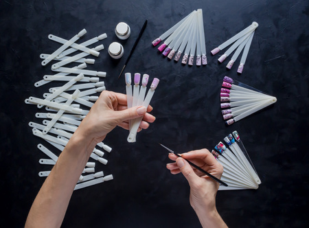 Nail art samples in female hands on the black table