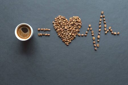 Love coffee concept. Heart from roasted coffee beans and cup of coffee on black background.の写真素材